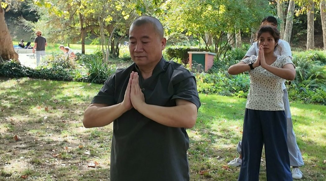 Maître Shi Heng Jun, mains jointes, pendant une séance de Qi Gong dans un parc