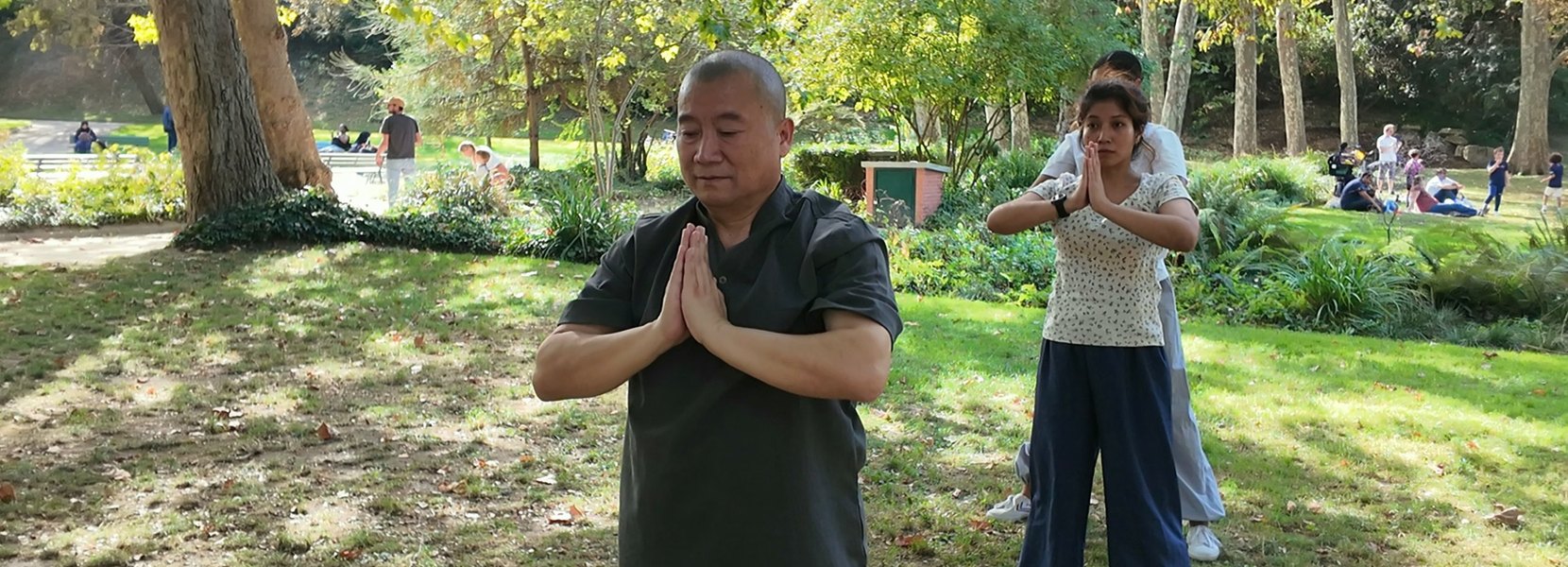 Maître Shi Heng Jun, mains jointes, pendant une séance de Qi Gong dans un parc