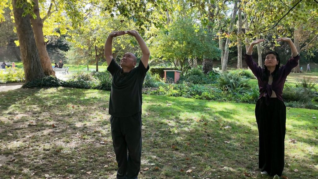 Maître Shi Heng Jun et l'instructrice Jingya Wei, bras levés au-dessus de la tête, pendant une séance de Qi Gong en plein air